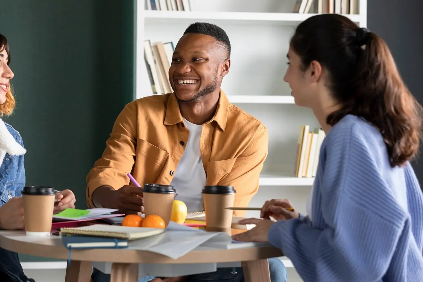 Ein junger Mann spricht mit seinen Freunden und macht während einer Lernsitzung Notizen.